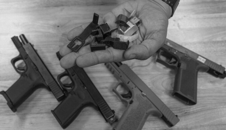 An ATF agent displays a handful of machine gun conversion devices, also known as auto sears, with an array of Glock-style pistols.