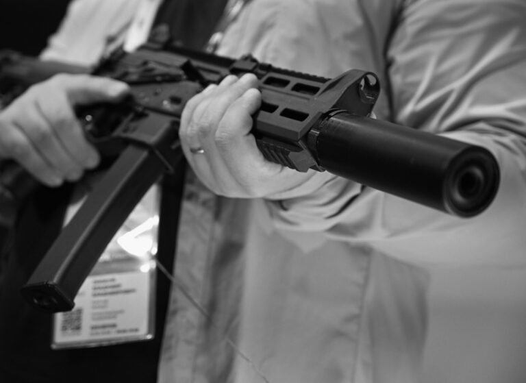 A man holds an AK-style rifle with a silencer at a trade show, at a time when silencer sales have spiked dramatically.