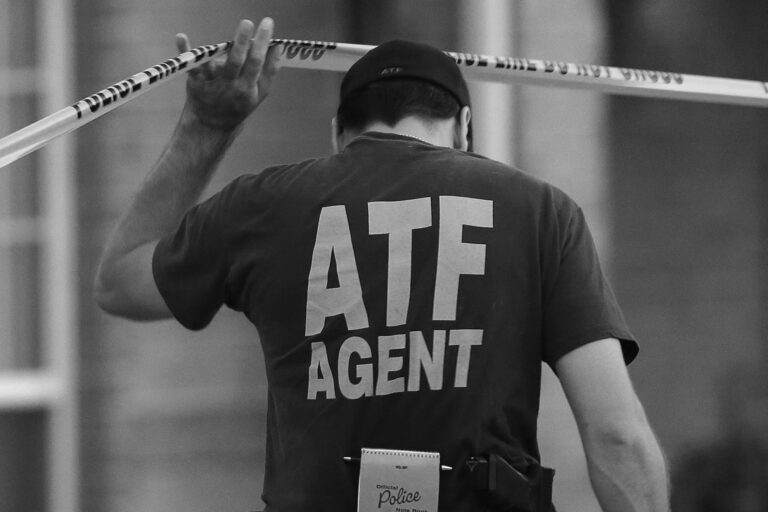 An ATF agent lifts crime scene tape after serving a warrant.