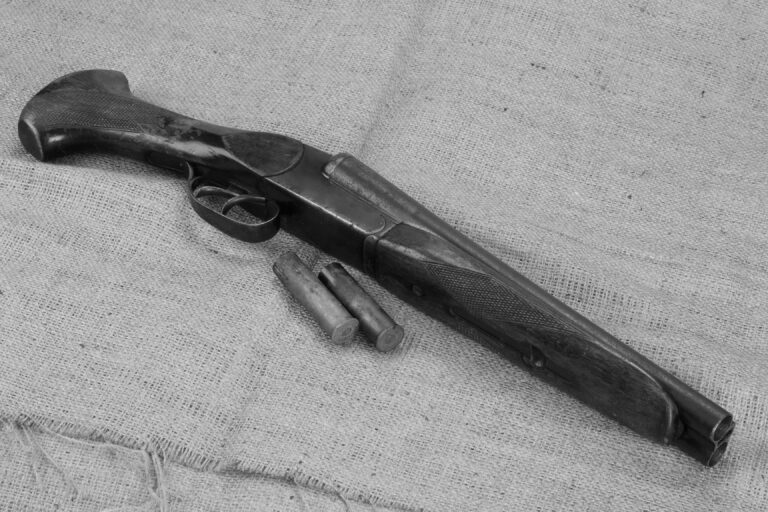 A sawed-off-shotgun that is considered a short-barreled shotgun under the NFA is shown with two shells.